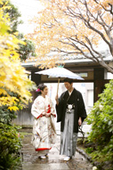 東京の撮影できる日本庭園で、紅葉の季節にウェディングフォトを撮る和傘を持つ和装の新郎とエスコートされる色打掛を着た新婦